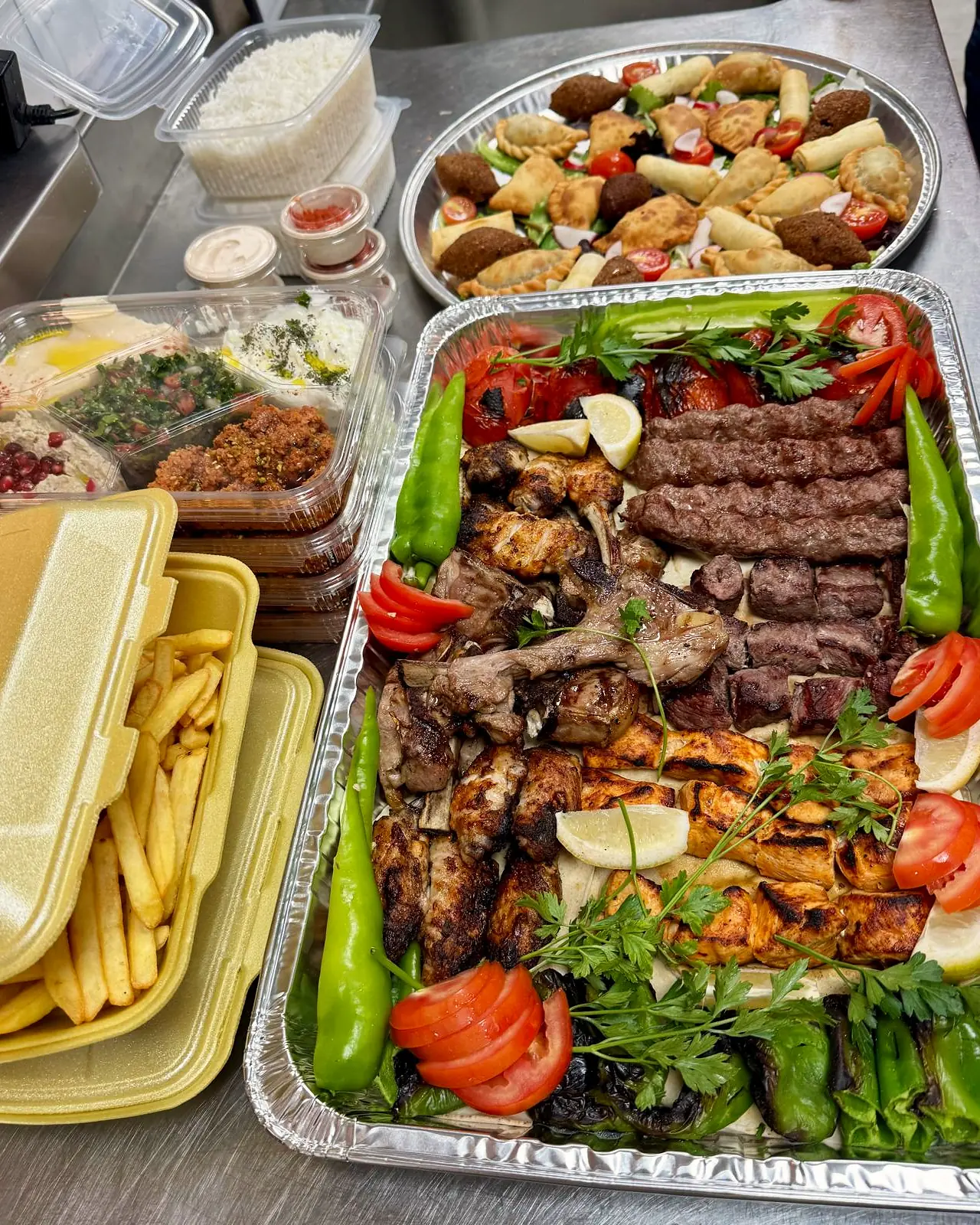Foil catering trays of grilled meats, mezza and fries ready to go