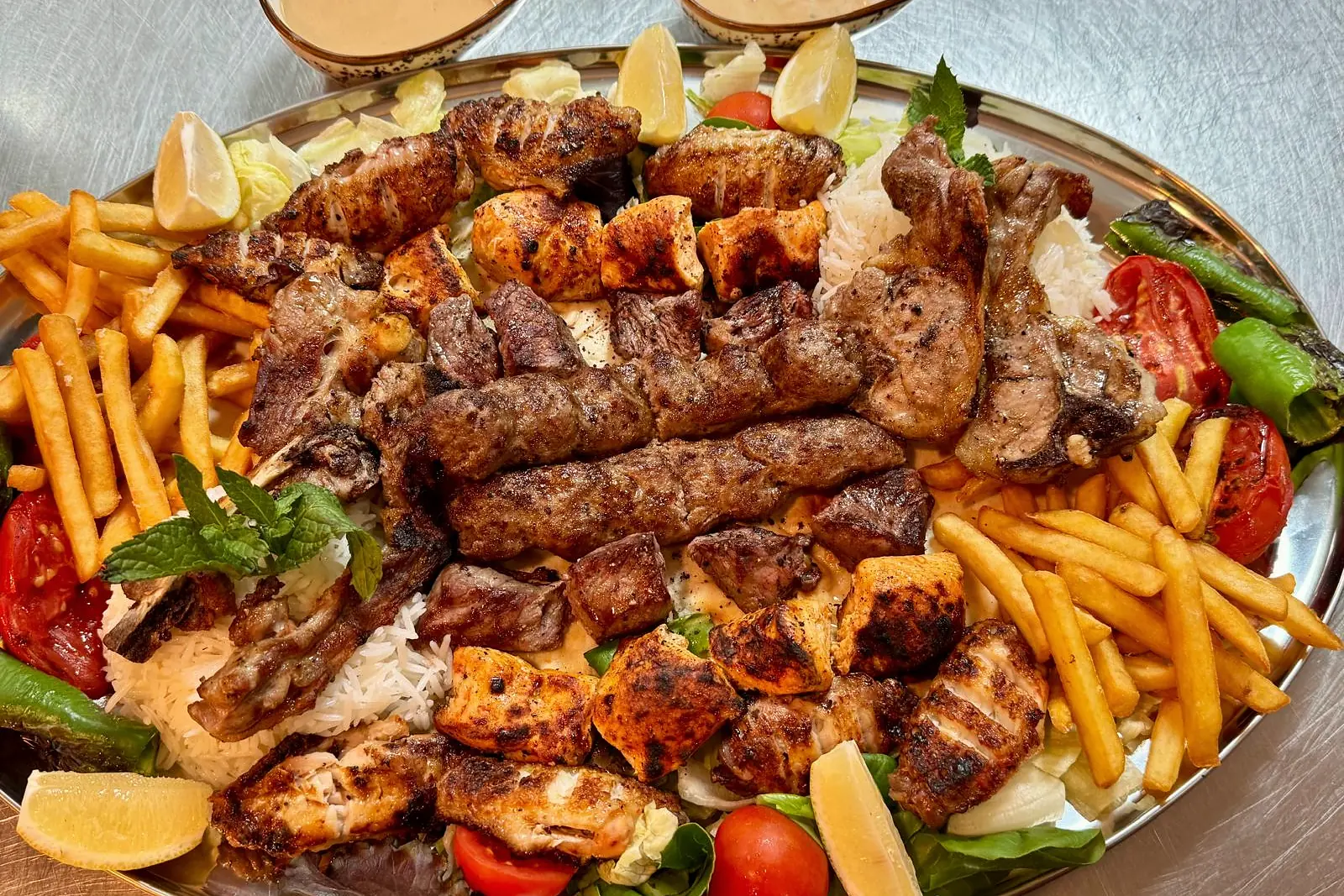 A platter of mixed charcoal-grilled meats with rice and fries